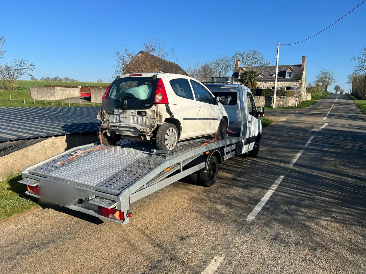 Peugeot 107 accidentée à l'arrière chargée sur plateau au bord d'une route de campagne