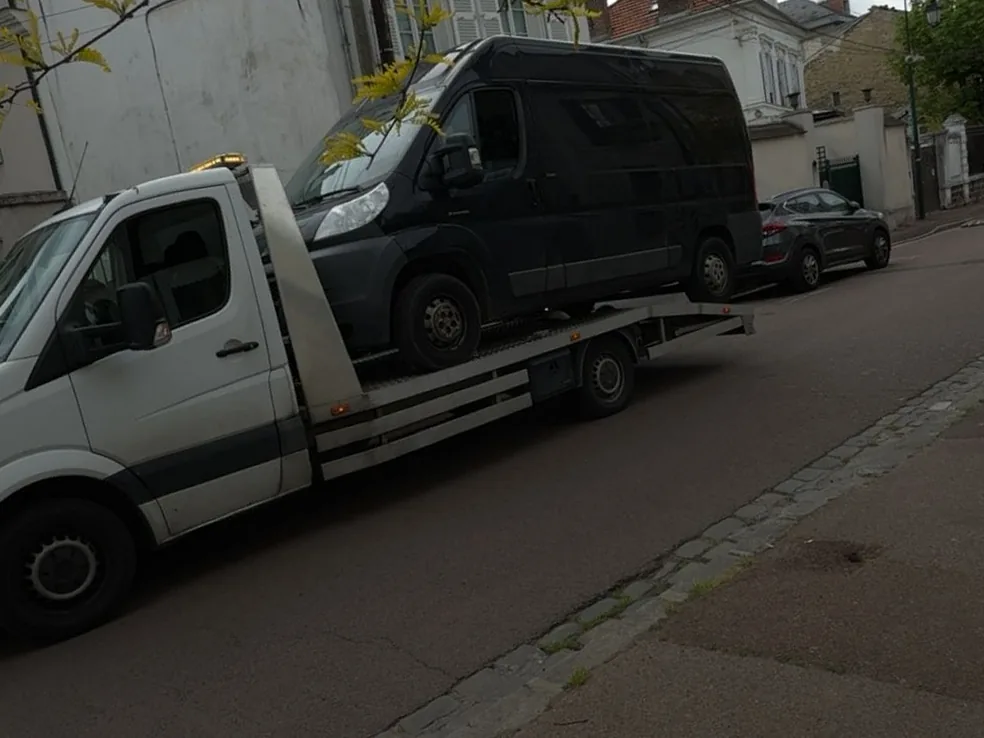 Fourgon noir chargé sur une dépanneuse plateau Mercedes Sprinter dans une rue résidentielle