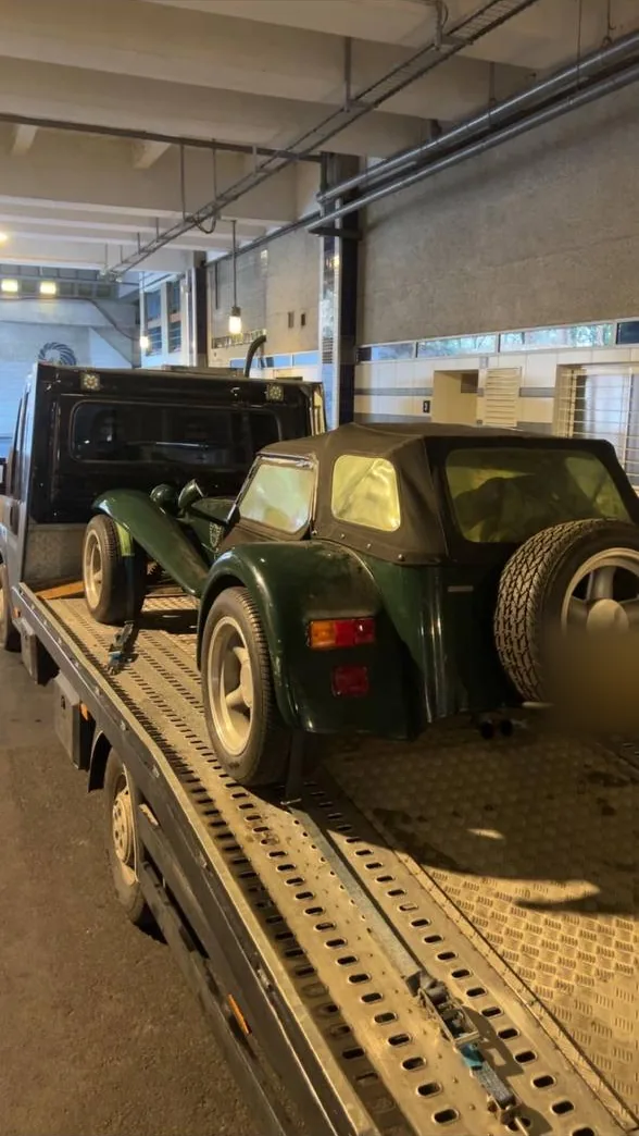 Roadster de collection type Seven chargé sur plateau dans un parking souterrain