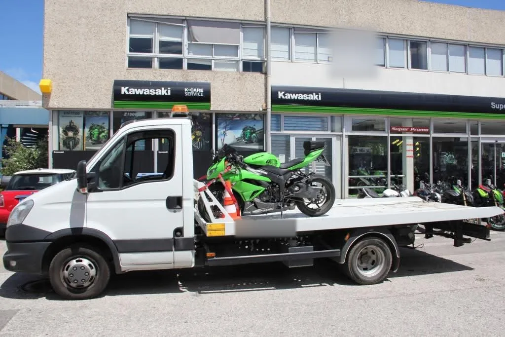 Moto Kawasaki Ninja verte sanglée sur une dépanneuse plateau Iveco Daily devant une concession Kawasaki
