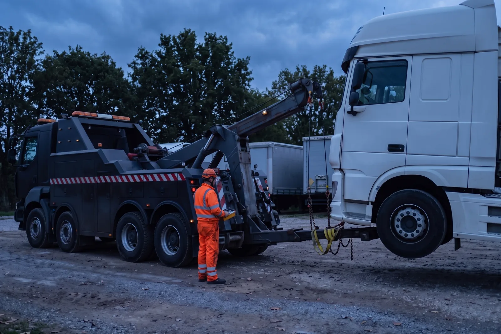 Dépanneuse lourde soulevant l'avant d'un tracteur routier en panne avec son bras de levage, manœuvrée par un dépanneur